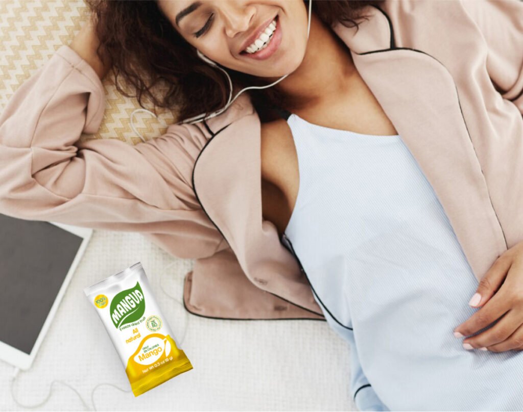Woman relaxing with earphones next to a Mangua freeze-dried mango bar, promoting healthy snacking and comfort.