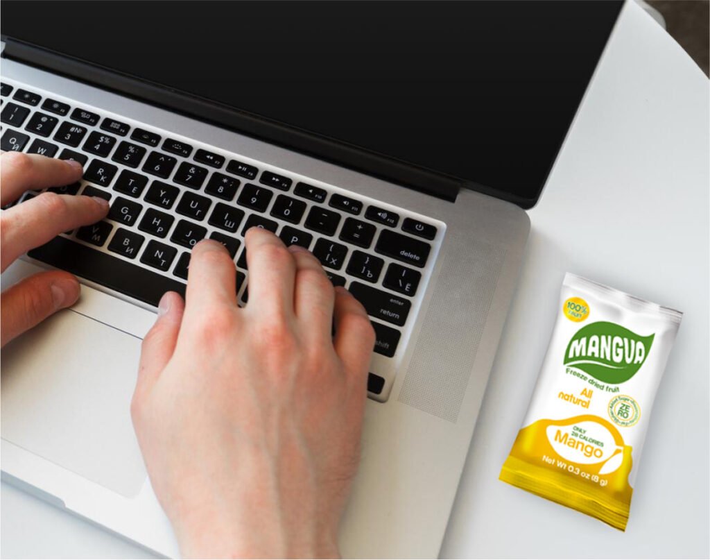 MANGUA freeze-dried mango snack on a desk next to a laptop during a work session.